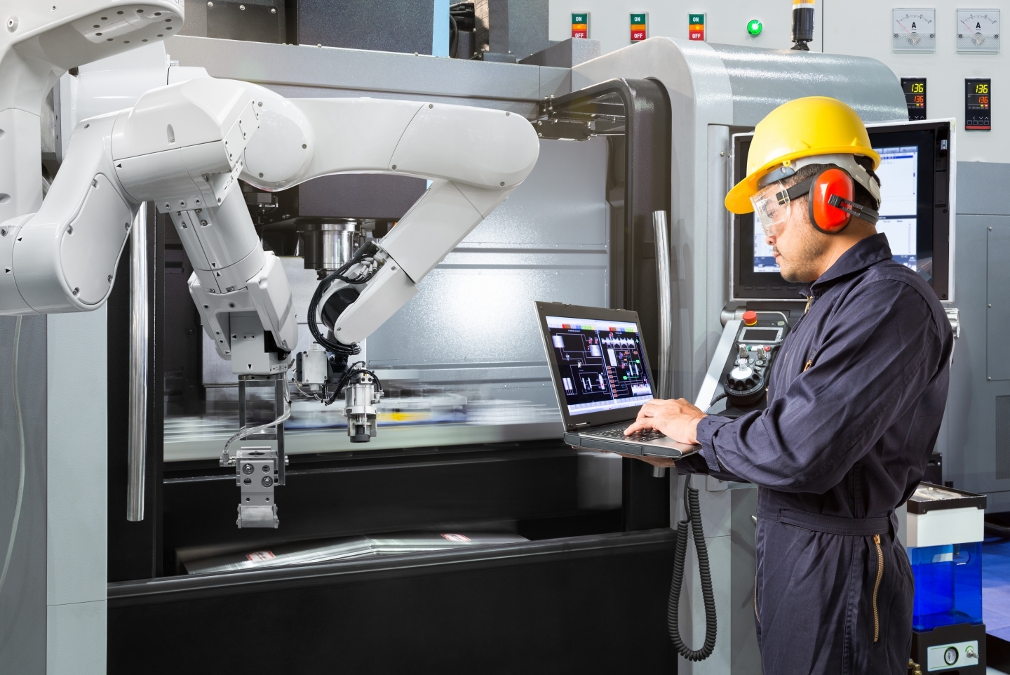 Maintenance engineer using laptop computer control automatic robotic hand with CNC machine in smart factory. (Source: Shutterstock)